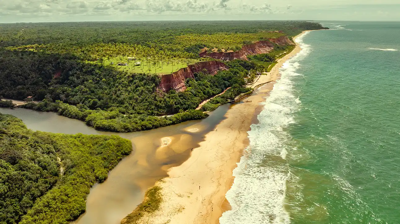 Vista aérea da Praia do Taipe em Trancoso, Bahia, destacando as falésias, o mar verde esmeralda e a vegetação nativa.