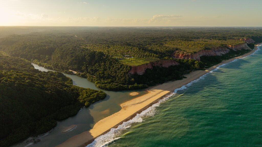 Vista aérea da Praia de Taípe, em Trancoso, Bahia, com falésias, o encontro do rio com o mar e a Mata Atlântica preservada